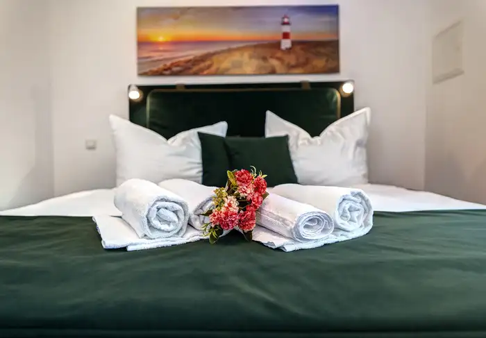 Frisch bezogenes Bett mit Handtüchern und Blume in der Ferienwohnung Ahlbeck
